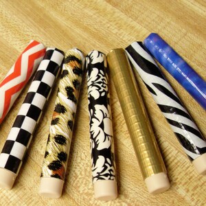 May include: Seven decorative sticks wrapped in different patterned paper. The patterns include chevron, checkered, leopard print, floral, gold, zebra print, and a blue and purple ombre pattern.