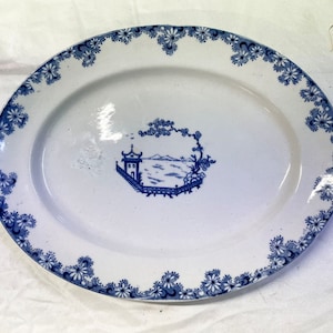 May include: Oval white serving platter with a blue floral border and a central blue landscape scene. The platter features a detailed design, suitable for serving food or as a decorative piece.