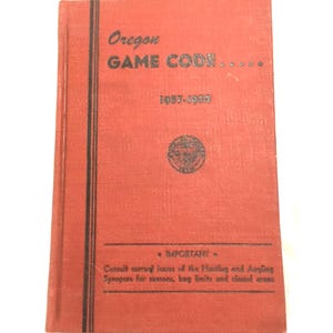 Puede incluir: Un libro rojo con el título "Oregon GAME CODE" y los años "1957-1958" impresos en la portada. El libro tiene líneas negras en el lomo y un pequeño sello en la portada. El texto "IMPORTANT" y "Consult current issues of the Hunting and Angling Synopses for seasons, bag limits and closed areas" está impreso en la parte inferior de la portada.