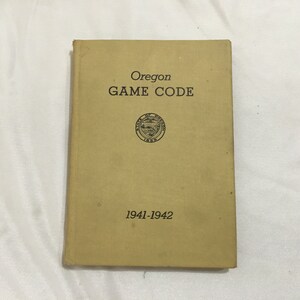 Puede incluir: Un libro de color beige titulado "Oregon GAME CODE" con el sello del estado y los años "1941-1942" impresos en la portada.