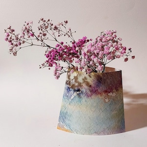 Könnte beinhalten: Ein Strauß rosa Gipskraut in einer bunten, abstrakt gemusterten Papier-Vase.