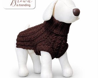 May include: A dark brown knitted dog sweater with a ribbed turtleneck collar and a textured cable knit pattern worn by a white dog mannequin. The image includes a white rectangular label with the text Brown is trending in brown script.