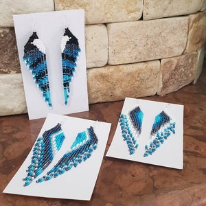 May include: Three pairs of beaded earrings on white cards. The earrings are made with blue, black, and white beads and are in the shape of a teardrop.