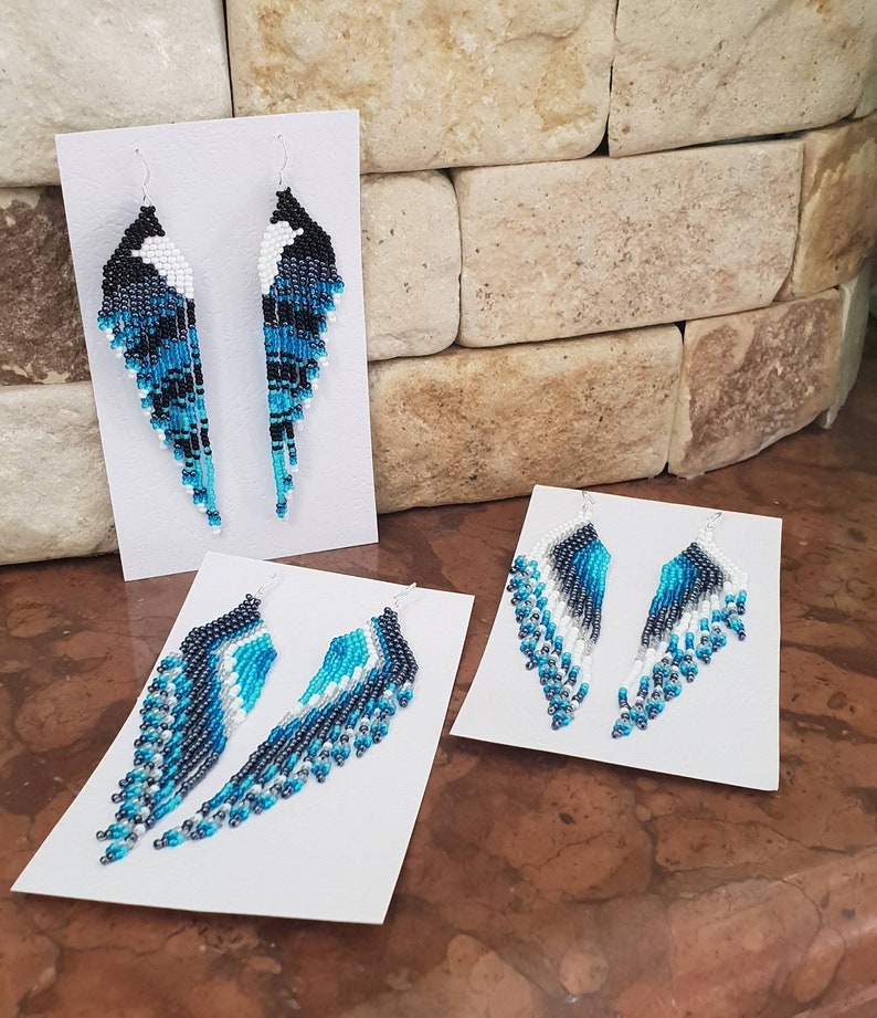 May include: Three pairs of beaded earrings on white cards. The earrings are made with blue, black, and white beads and are in the shape of a teardrop.