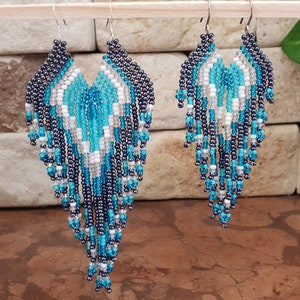 May include: A pair of long, beaded earrings with a teardrop shape. The earrings are made with black, white, and turquoise beads.