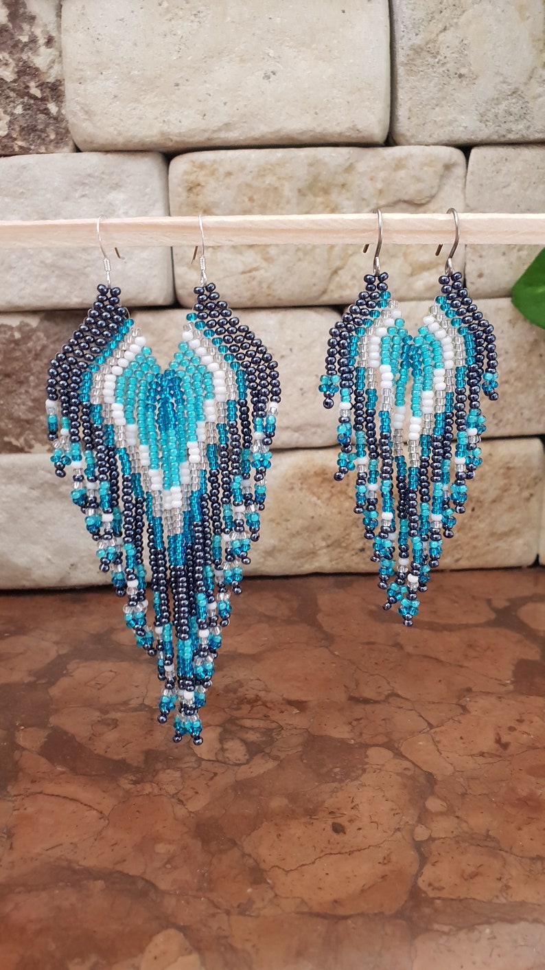 May include: A pair of long, beaded earrings with a teardrop shape. The earrings are made with black, white, and turquoise beads.