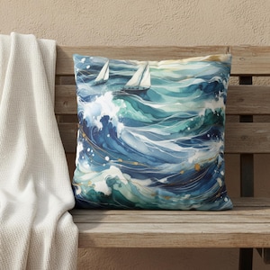 Peut inclure: Coussin carré décoratif avec un motif aquarelle de vagues océaniques dans des tons de bleu et de vert d'eau. Deux voiliers sont visibles sur l'eau. Des accents dorés ajoutent des détails aux vagues. Le coussin est posé sur un banc en bois.