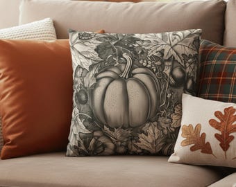 May include: A collection of decorative throw pillows in autumnal colors. The central pillow features a detailed grayscale illustration of a pumpkin surrounded by leaves. Other pillows are solid orange, plaid, and a cream-colored pillow with embroidered leaves.