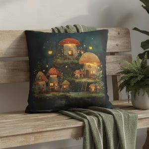 Op de afbeelding: Een vierkant decoratief kussen met een fantasie-illustratie van paddenstoelhuizen in een bos. Het ontwerp heeft een donkerblauwe achtergrond met gloeiende lichten en een kleurenpalet van groen en oranje. Het kussen ligt op een houten bank.