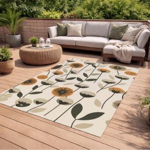 Könnte beinhalten: Ein rechteckiger Outdoor-Teppich mit floralem Muster. Der Teppich hat einen cremefarbenen Hintergrund mit stilisierten Blumen in Orange, Schwarz und Grau sowie dunkelgrünen Blättern. Der Teppich liegt auf einer Holzterrasse, mit Gartenmöbeln im Hintergrund.