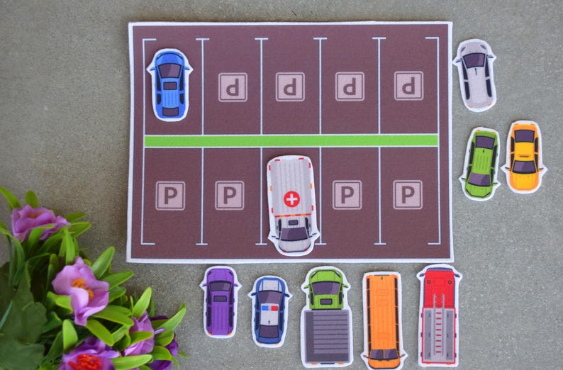 May include: A brown and green parking lot play mat with a white ambulance, a blue car, a green car, a yellow car, a purple car, a police car, a truck, a school bus, and a fire truck. The mat has the letters 'P' and 'D' printed on it.