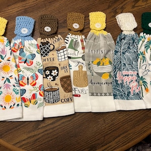 May include: Set of seven kitchen towels with crocheted loops and buttons. The towels feature various designs including coffee, lemons, flowers, and palm trees. The text on the towels includes "Coffee", "Happiness is Homemade", "This is my Happy Place", and "Hello Sunshine".