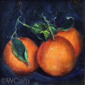 May include: Three bright orange oranges with green leaves on a dark blue background. The oranges are arranged in a still life composition.