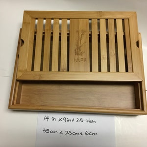May include: A rectangular bamboo tea tray with a slatted top and a pull-out drawer. The tray measures 14 inches long, 9 inches wide, and 2.5 inches high. The top has a bamboo design with a bamboo illustration and text.