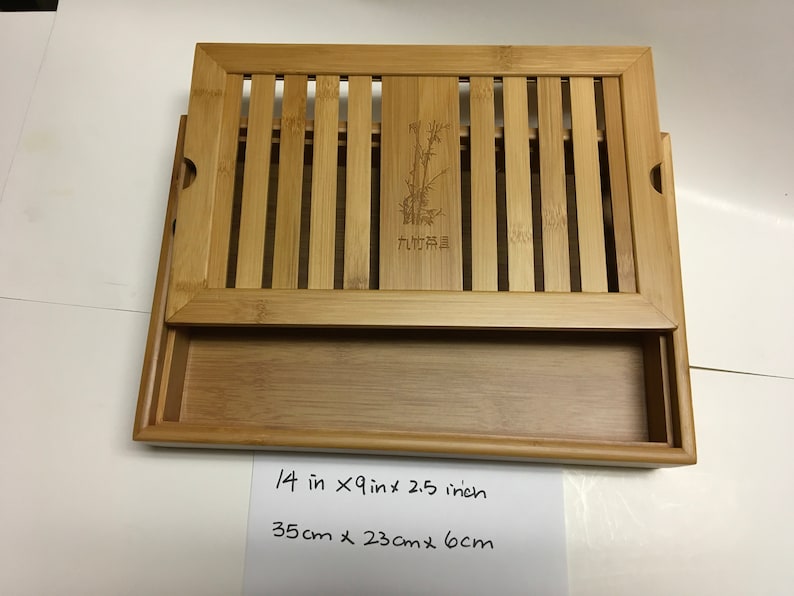 May include: A rectangular bamboo tea tray with a slatted top and a pull-out drawer. The tray measures 14 inches long, 9 inches wide, and 2.5 inches high. The top has a bamboo design with a bamboo illustration and text.