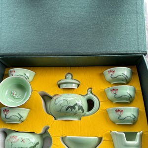 May include: A green and white porcelain tea set with a lotus flower design. The set includes a teapot, a lid, a teacup, and a small bowl. The set is in a yellow box.
