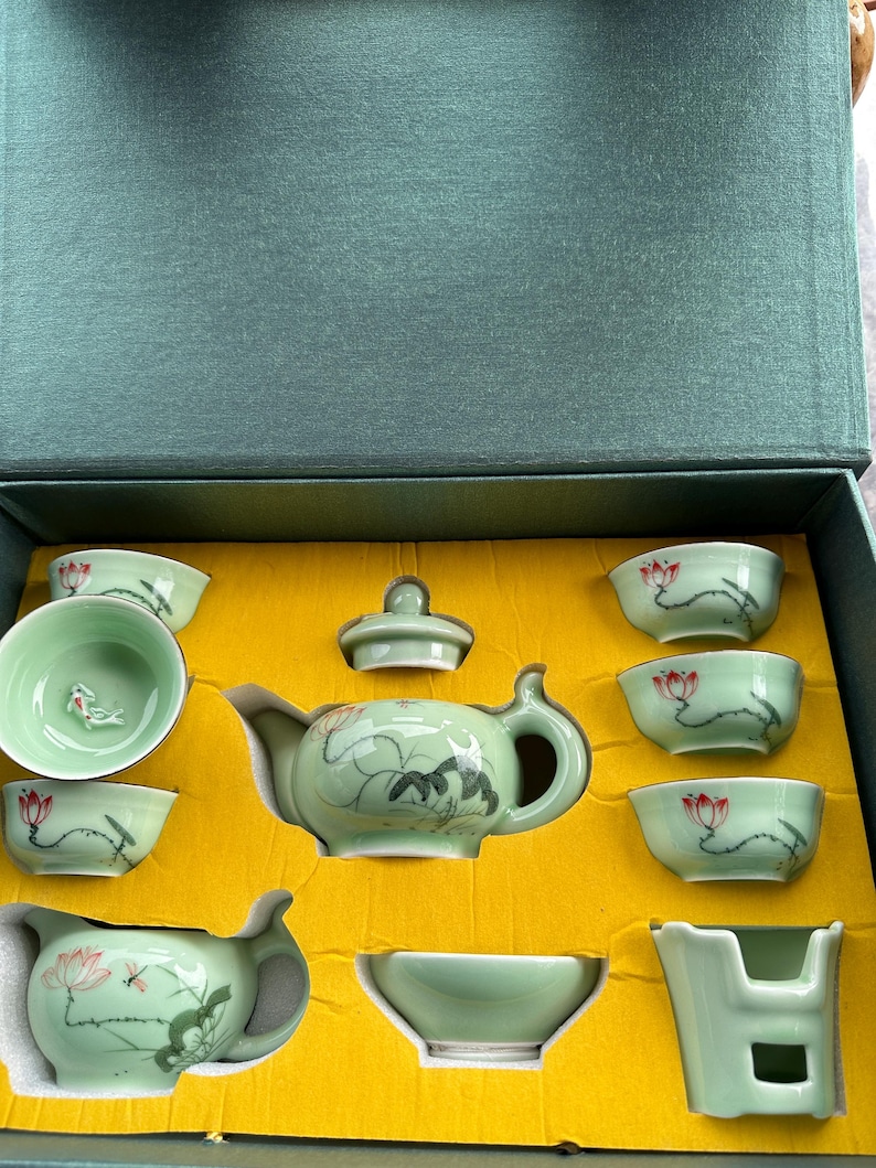 May include: A green and white porcelain tea set with a lotus flower design. The set includes a teapot, a lid, a teacup, and a small bowl. The set is in a yellow box.