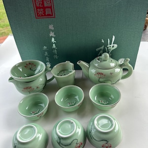 May include: A green tea set with a teapot, a strainer, and six cups. The set is decorated with a lotus flower design. The box is green and has Chinese characters on it.