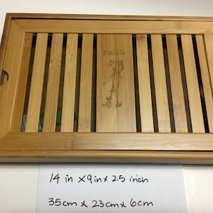 May include: Rectangular bamboo tea tray, 14 inches long, 9 inches wide, and 2.5 inches high. The tray features a slatted design with a central panel etched with a bamboo plant and Chinese characters. The tray has rounded corners and handles.