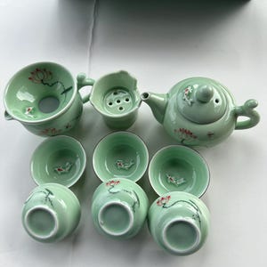 May include: A green tea set with a teapot, a strainer, and six cups. The cups and teapot are decorated with red and white flowers and fish.