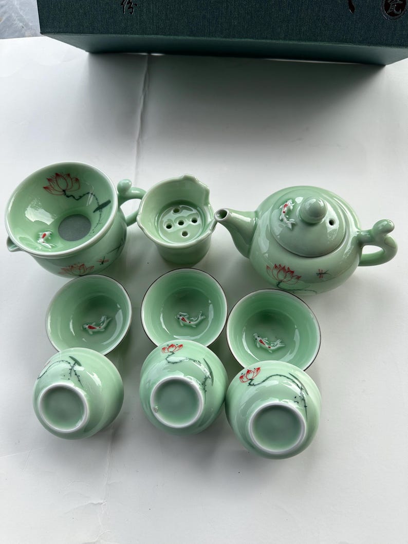 May include: A green tea set with a teapot, a strainer, and six cups. The cups and teapot are decorated with red and white flowers and fish.
