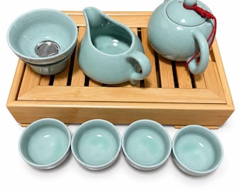 May include: A light blue ceramic tea set featuring a teapot with a red cord, a pitcher, a strainer, and four small cups arranged on a rectangular bamboo tray. The ceramic pieces have a visible crackle glaze finish throughout the entire set.