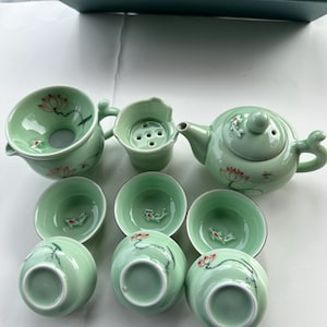 May include: A green tea set with a teapot, infuser, and six cups. The teapot and cups feature a delicate floral design with red accents.