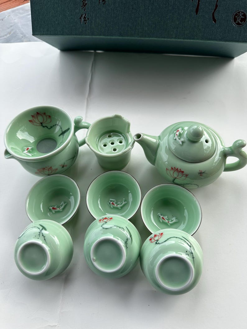 May include: A green tea set with a teapot, infuser, and six cups. The teapot and cups feature a delicate floral design with red accents.