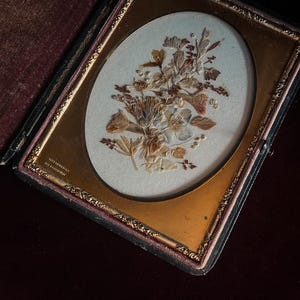 May include: A vintage pressed flower display in a gold frame with a black velvet mat. The frame has a gold inscription that reads "Copyright 1897, Geo. F. Gregory".