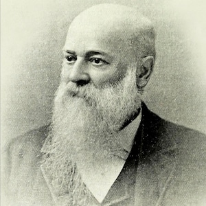 May include: Black and white portrait of a man with a long white beard and a bald head. He is wearing a dark suit and a white shirt.