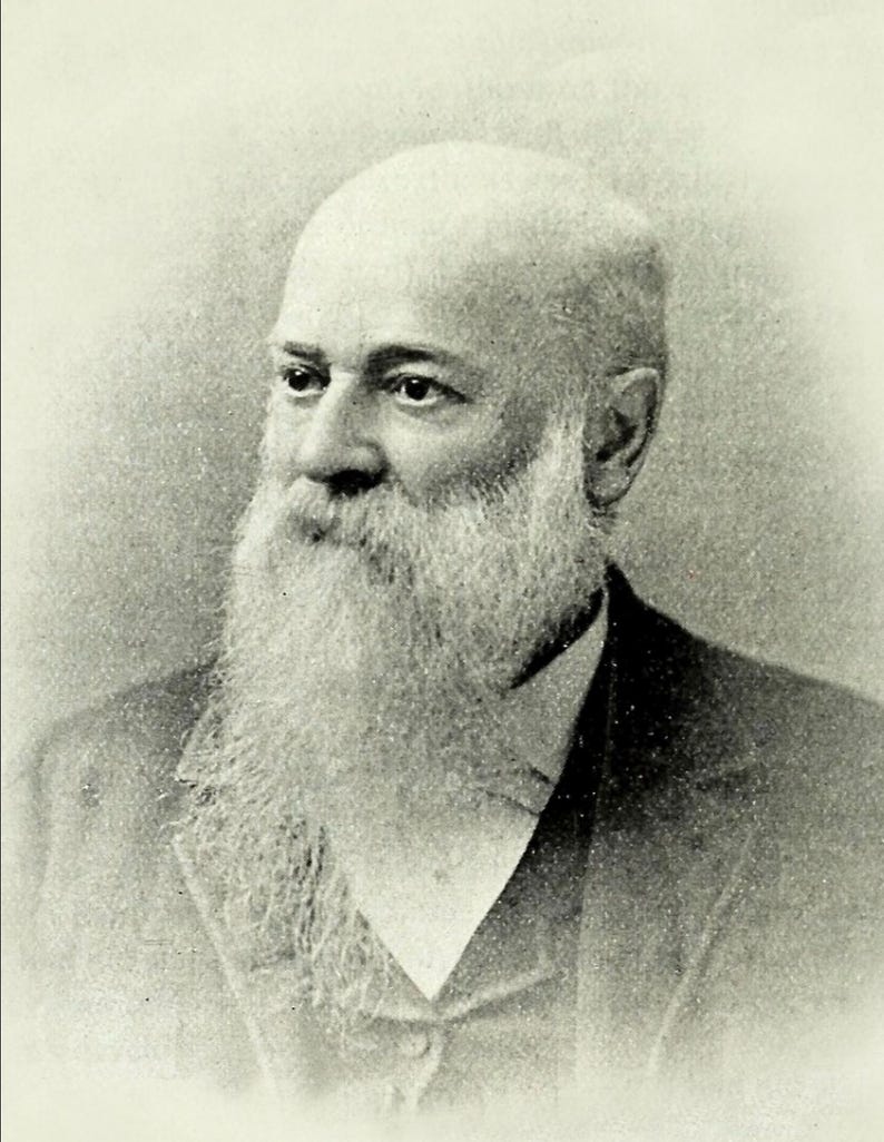 May include: Black and white portrait of a man with a long white beard and a bald head. He is wearing a dark suit and a white shirt.