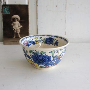 Może przedstawiać: Biała ceramiczna miska z niebieskim, żółtym i zielonym wzorem kwiatowym. Miska ma falisty brzeg i zaokrąglone dno.