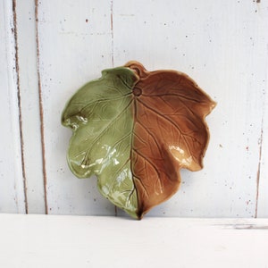 May include: A ceramic leaf-shaped serving dish with a green and brown glaze. The dish is shaped like a single leaf with a raised vein pattern.