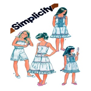 May include: A vintage Simplicity sewing pattern for girls' sleepwear. The pattern includes four different styles: a dress with a ruffled hem, a skirt with a ruffled hem, a pair of shorts with a lace trim, and a dress with a ruffled hem and a bow at the waist. The pattern is illustrated with four girls wearing the different styles of sleepwear.