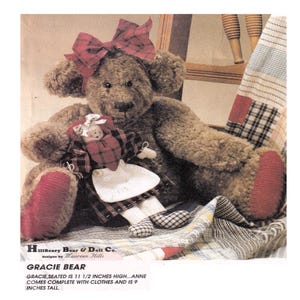 Puede incluir: Un oso de peluche marrón hecho a mano con un lazo a cuadros rojo y detalles rojos en las patas. El oso sostiene una muñeca pequeña con un corazón rojo y un vestido a cuadros. El texto dice "Gracie Bear" y "Gracie, sentado mide 29 cm de alto...Anne viene completa con ropa y mide 23 cm de alto."