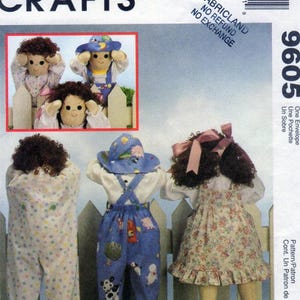 Op de afbeelding: Een McCall's Crafts 9605 naaipatroon-envelop met drie poppen met bruin haar. Eén pop draagt een witte slaapzak met stippen, één draagt een blauwe tuinbroek met dierenprints en een bijpassende hoed, en één draagt een bloemetjesjurk met roze strik.