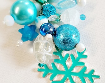May include: A teal and white snowflake charm with a silver ring. The charm is decorated with various beads, including teal, white, and blue beads.