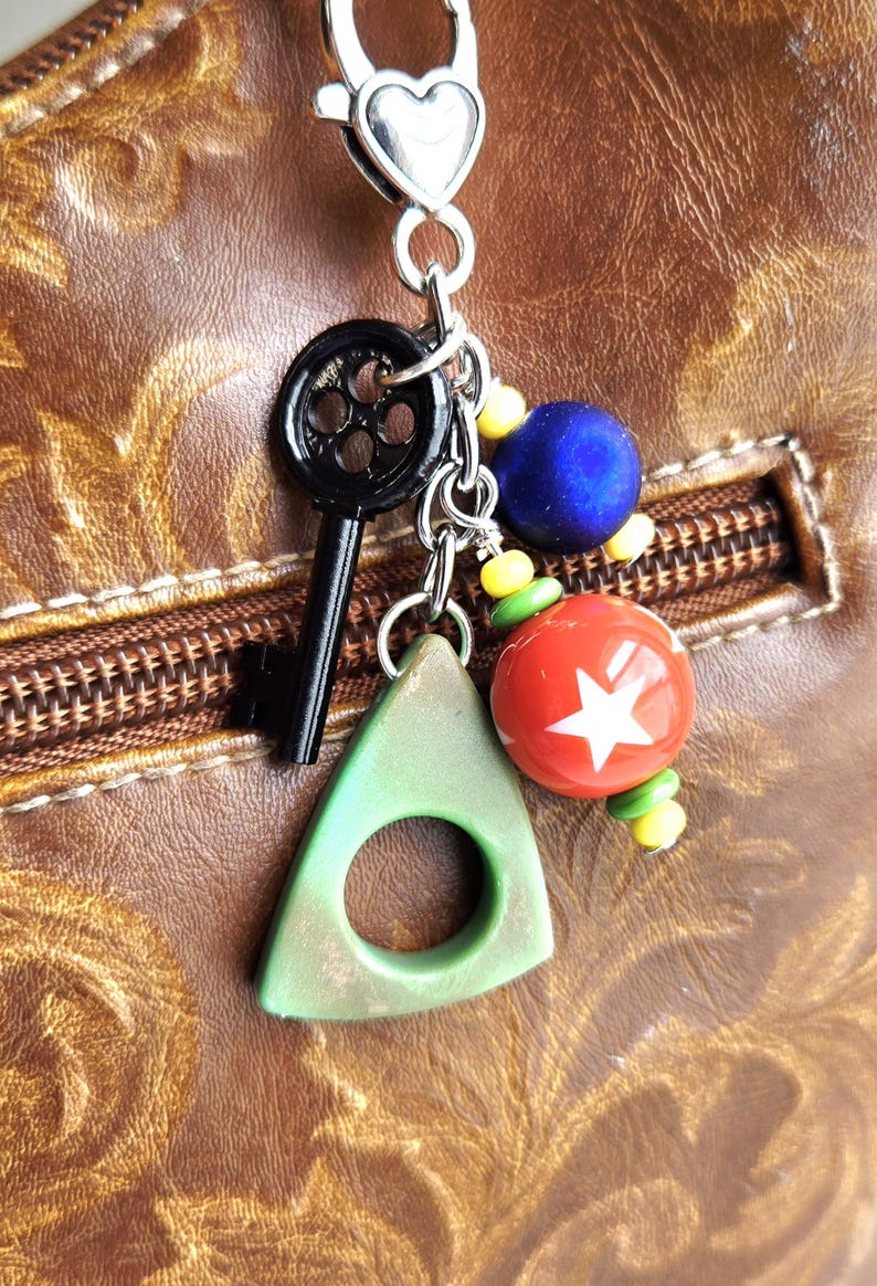 May include: A silver keychain with a heart-shaped clasp, featuring a black key, a green triangle with a hole, and colorful beads. A red bead with a white star is also included.