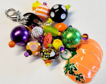 May include: A Halloween-themed charm with a pumpkin, spiderweb, and other colorful beads. The charm is attached to a silver lobster clasp.