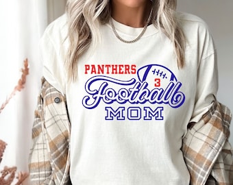 Könnte beinhalten: Weißes Langarm-T-Shirt mit blauem und rotem Text, der "Panthers Football Mom" lautet, und einer blauen und weißen Football-Grafik mit der Nummer "3" in Rot.