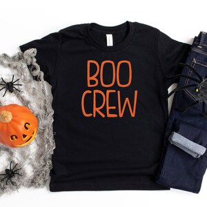 May include: Black t-shirt with the text "BOO CREW" in orange lettering. The shirt is on a white surface with a spider web and a pumpkin.