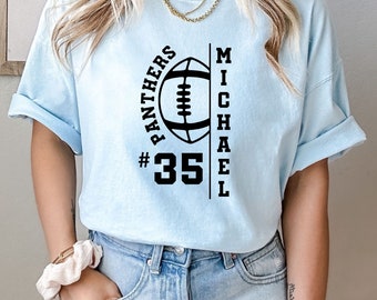 Könnte beinhalten: Hellblaues T-Shirt mit schwarzer Football-Grafik. Das Shirt zeigt den Text "PANTHERS" über einem Football, die Nummer "35" und den Namen "MICHAEL". Das T-Shirt besteht aus einem weichen Material.