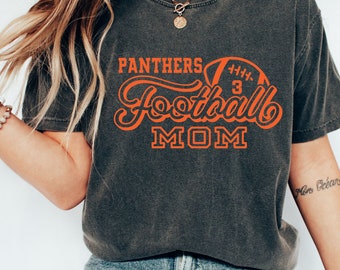 Könnte beinhalten: Dunkelgraues T-Shirt mit dem Schriftzug "Panthers Football Mom" in Orange und einer Football-Grafik. Das Shirt hat einen Rundhalsausschnitt und kurze Ärmel.