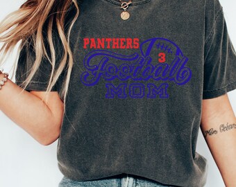 Könnte beinhalten: Ein dunkelgraues T-Shirt mit dem Text "Panthers Football Mom" in blauer und roter Schrift. Der Text ist mit einer Fußballgrafik gestaltet.