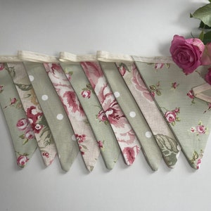 May include: A green and pink floral bunting with white polka dots. The bunting is made of fabric and has a white lace trim.