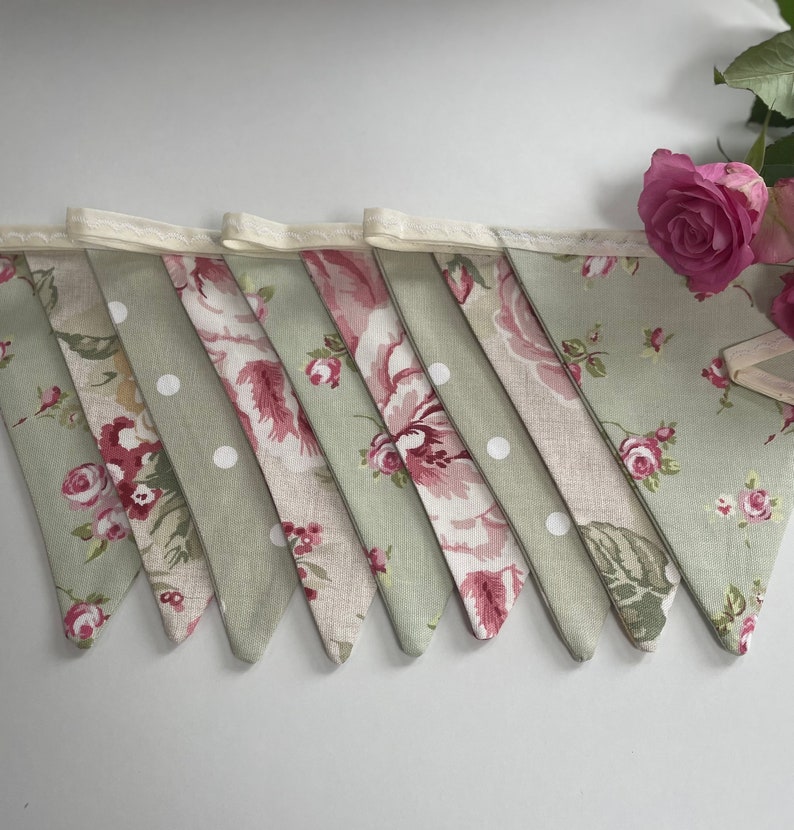 May include: A green and pink floral bunting with white polka dots. The bunting is made of fabric and has a white lace trim.