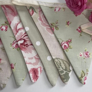 May include: A green and pink floral bunting with white polka dots. The bunting is made of fabric and has a cream-colored trim.