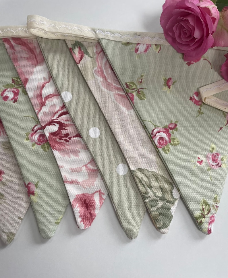 May include: A green and pink floral bunting with white polka dots. The bunting is made of fabric and has a cream-colored trim.