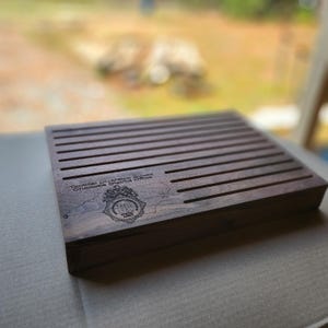 May include: A dark brown wooden coin display case with slots for coins. The case is engraved with the text "Tactical Diversion Squad Charlotte District Office" and a police badge.