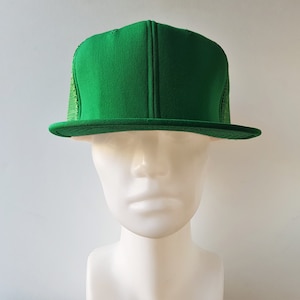 Puede incluir: Gorra de camionero verde brillante con visera plana y parte trasera de malla. La gorra tiene un panel frontal estructurado y un cierre a presión. La gorra se muestra en una cabeza de maniquí blanca sobre un fondo blanco.